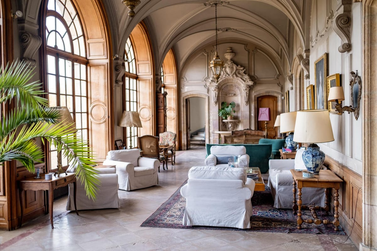 Grand chateau salon with barrel-vaulted ceilings, baroque moldings, white armchairs, and Persian rug