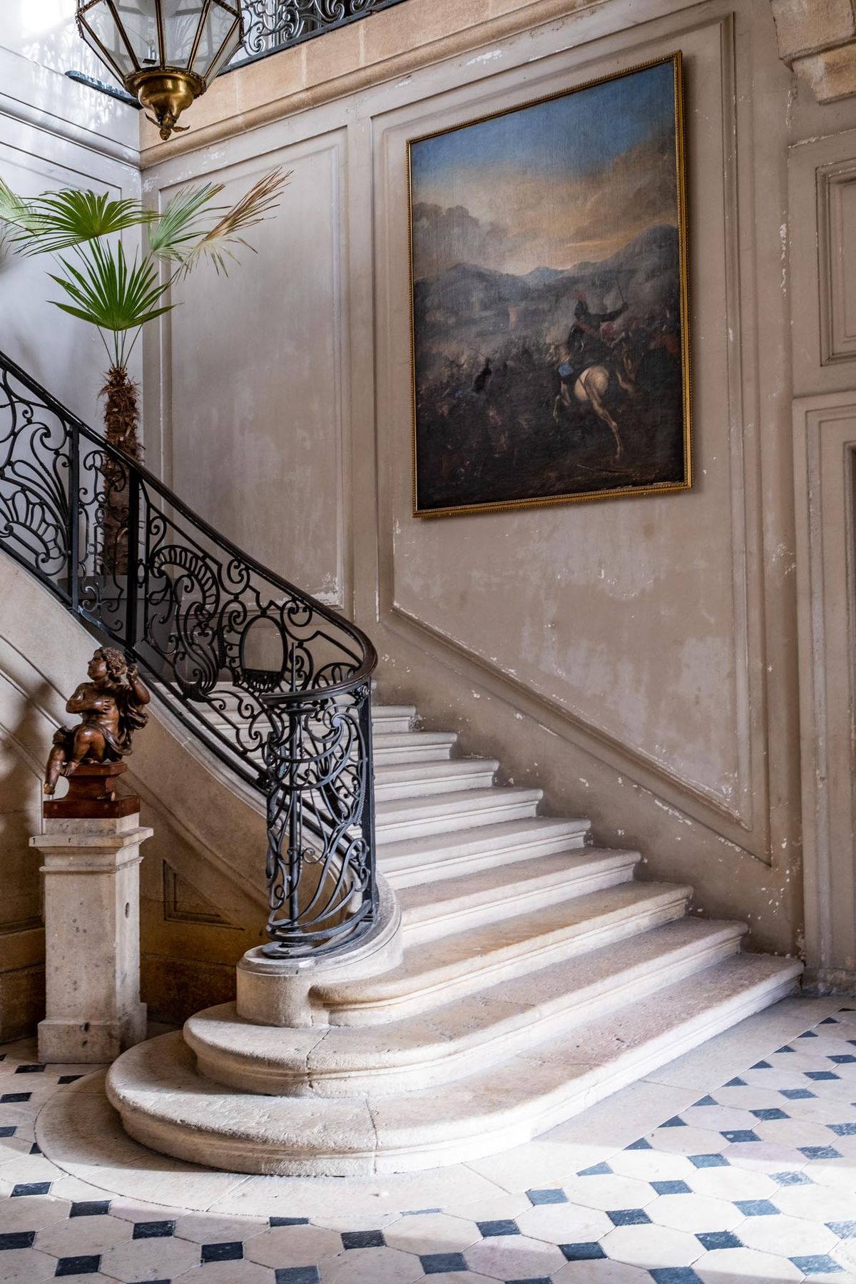 Chateau entrance hall with curved stone staircase wrought-iron balustrade and battle painting