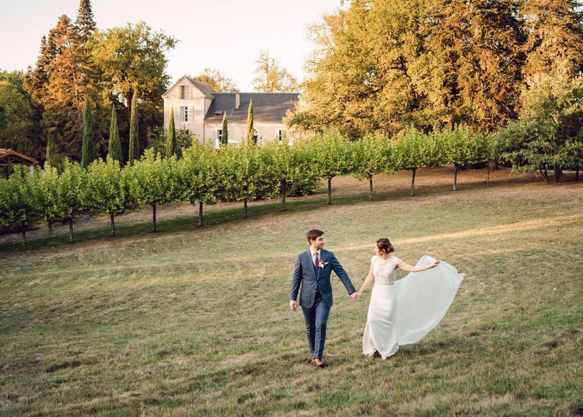 Couple walking across lawn with bride fanning gown skirt in golden hour light before country estate
