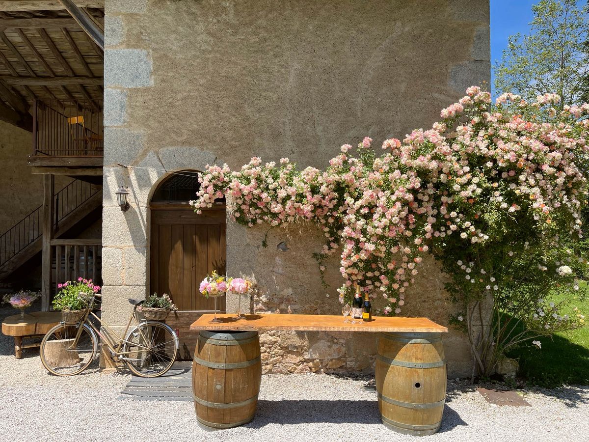 Wine barrel bar with Veuve Clicquot, vintage bicycle, and pink peonies at climbing rose-framed doorway