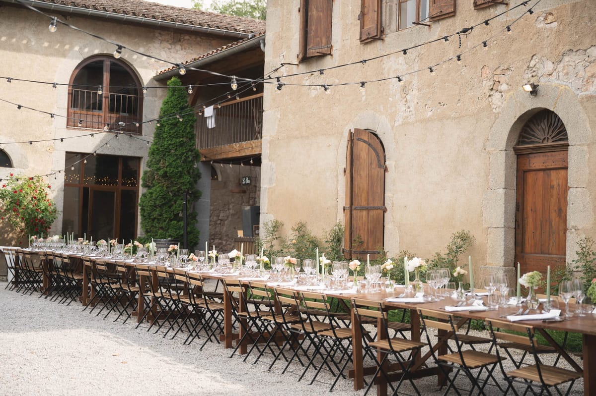 Parallel farm tables with peach roses, sage tapers, and bistro chairs in rustic stone farmhouse courtyard