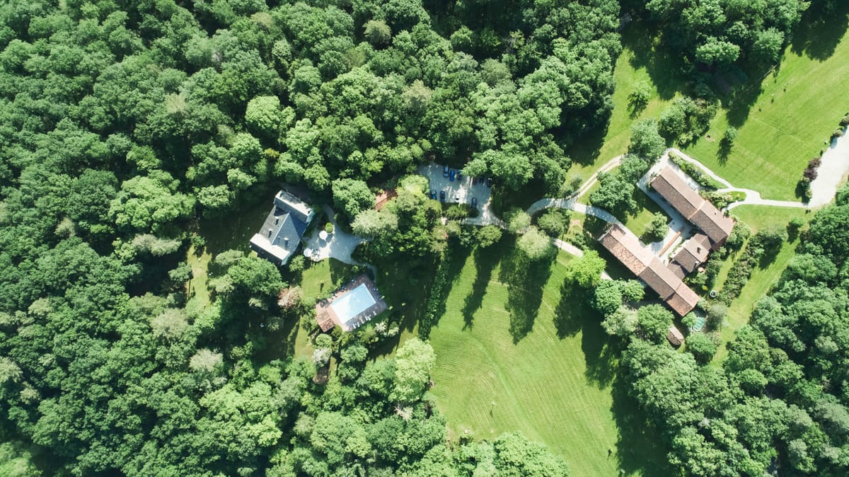 Aerial drone shot of French country estate with manor house, swimming pool, outbuildings, and wooded grounds