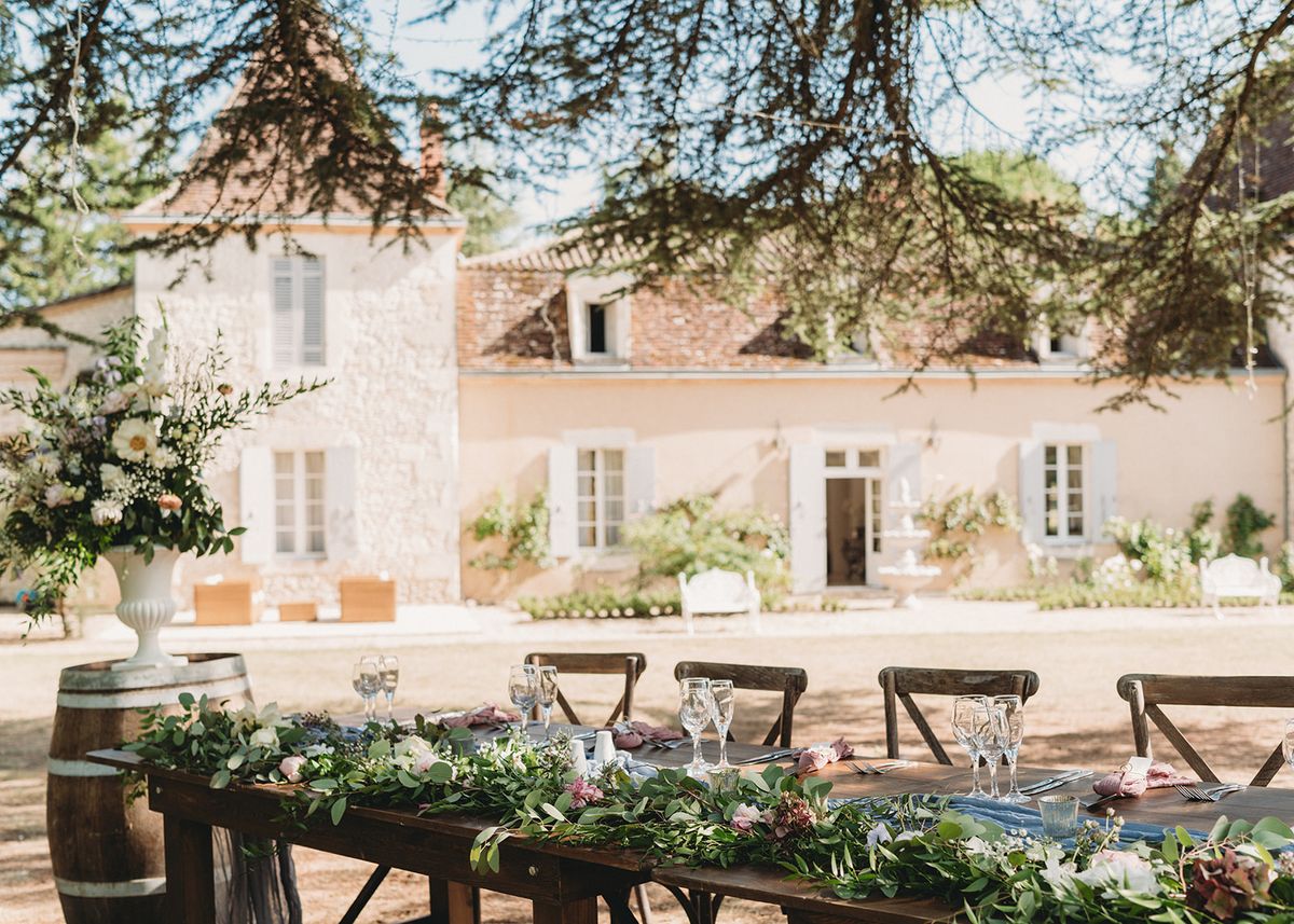 Farm table with eucalyptus garland and blush blooms before French manor with blue shutters