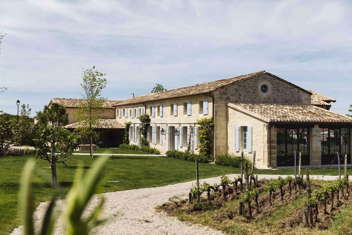 Two-storey limestone farmhouse with terracotta roof, blue shutters, glass conservatory extension, and gravel drive with gr...