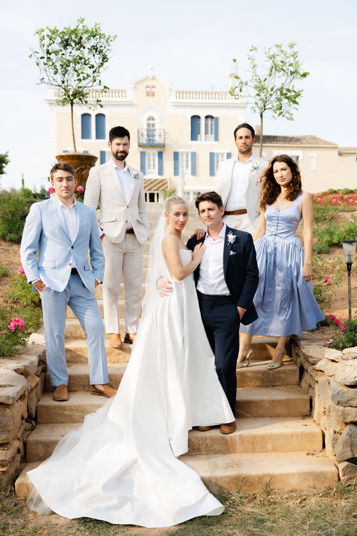 Bride and groom with four wedding party members on stone steps of a yellow Provencal villa with blue shutters