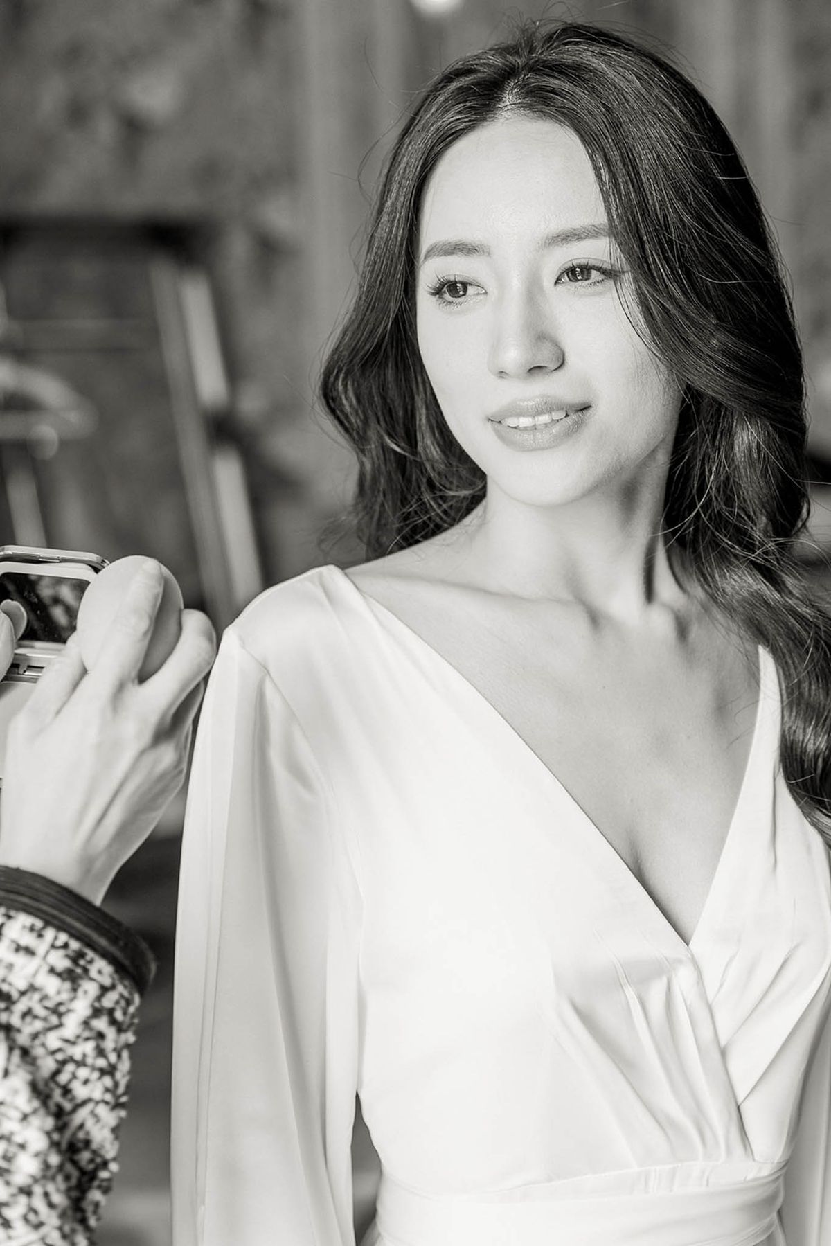 Black and white close-up of bride in white wrap robe during hair and makeup preparation