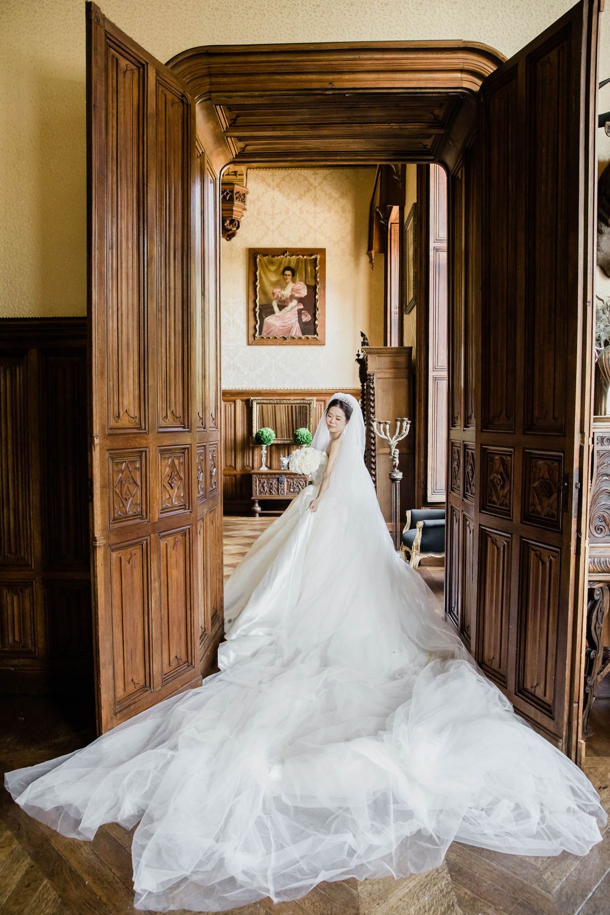 Bride in tulle ballgown with diamond tiara and cathedral train standing in carved walnut chateau doorway