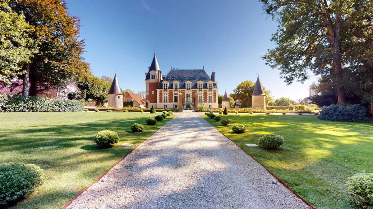 Red brick and cream stone chateau with slate mansard roof, turrets, and box-hedge-lined gravel drive