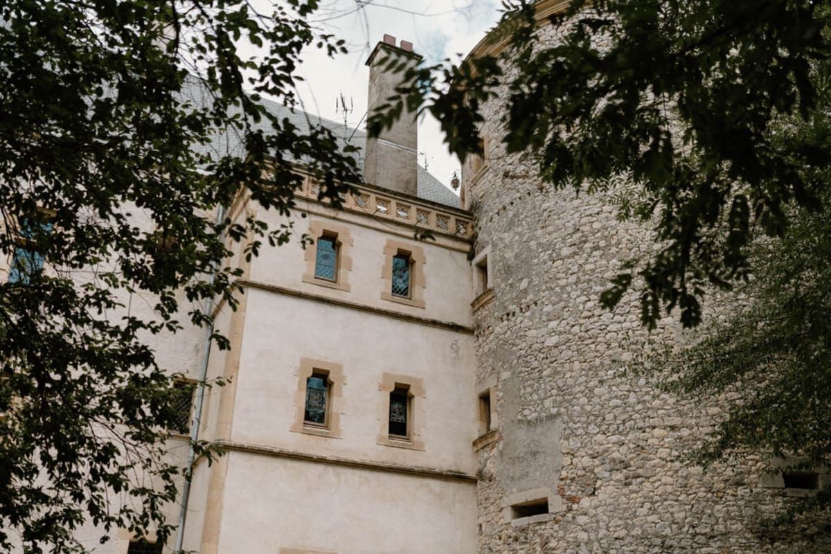 Upward-angled shot of cream chateau facade with stone-framed arched windows and medieval round tower