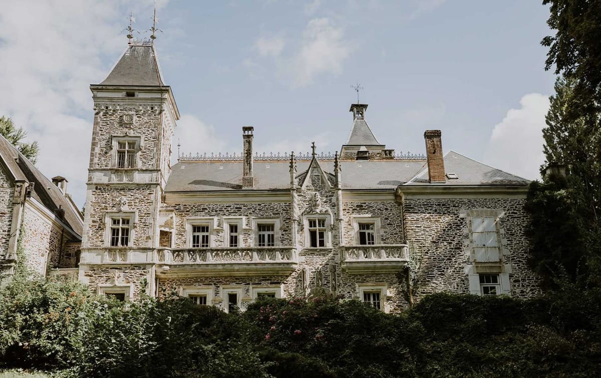 Multi-storey stone chateau with pointed turret, iron cresting, and white stone balustrades from grounds
