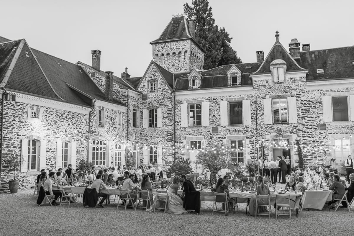 Black and white elevated view of chateau courtyard reception with 60-80 guests under string lights at evening