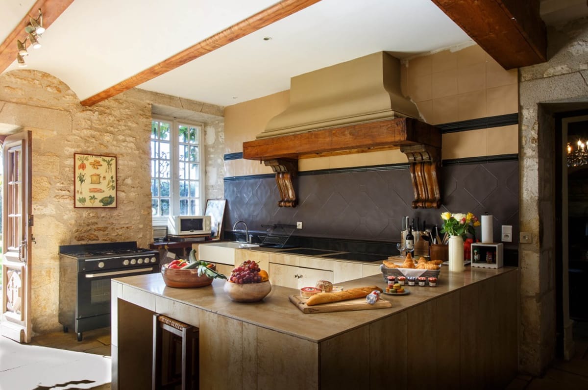 Rustic French chateau kitchen with stone walls, wooden beams, and breakfast spread on stone-topped island