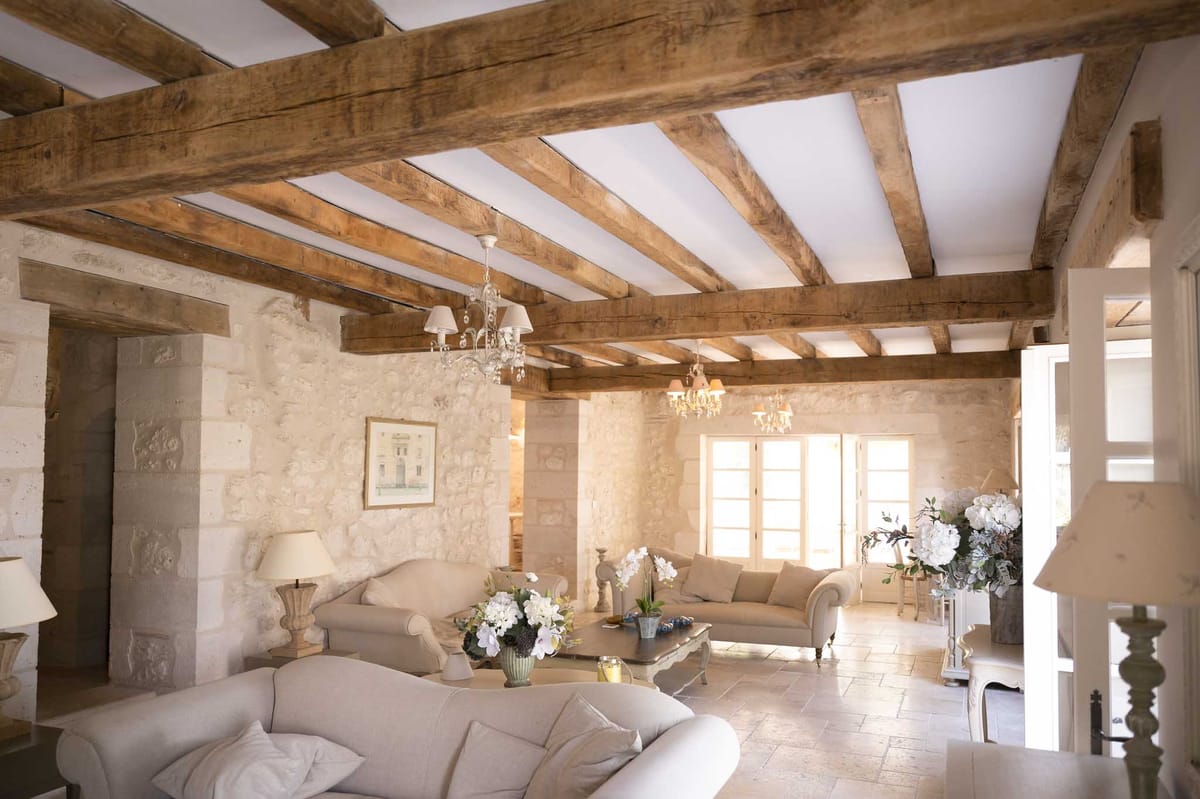 French country salon with exposed beams, cream linen sofas, crystal chandeliers, and white hydrangea arrangements