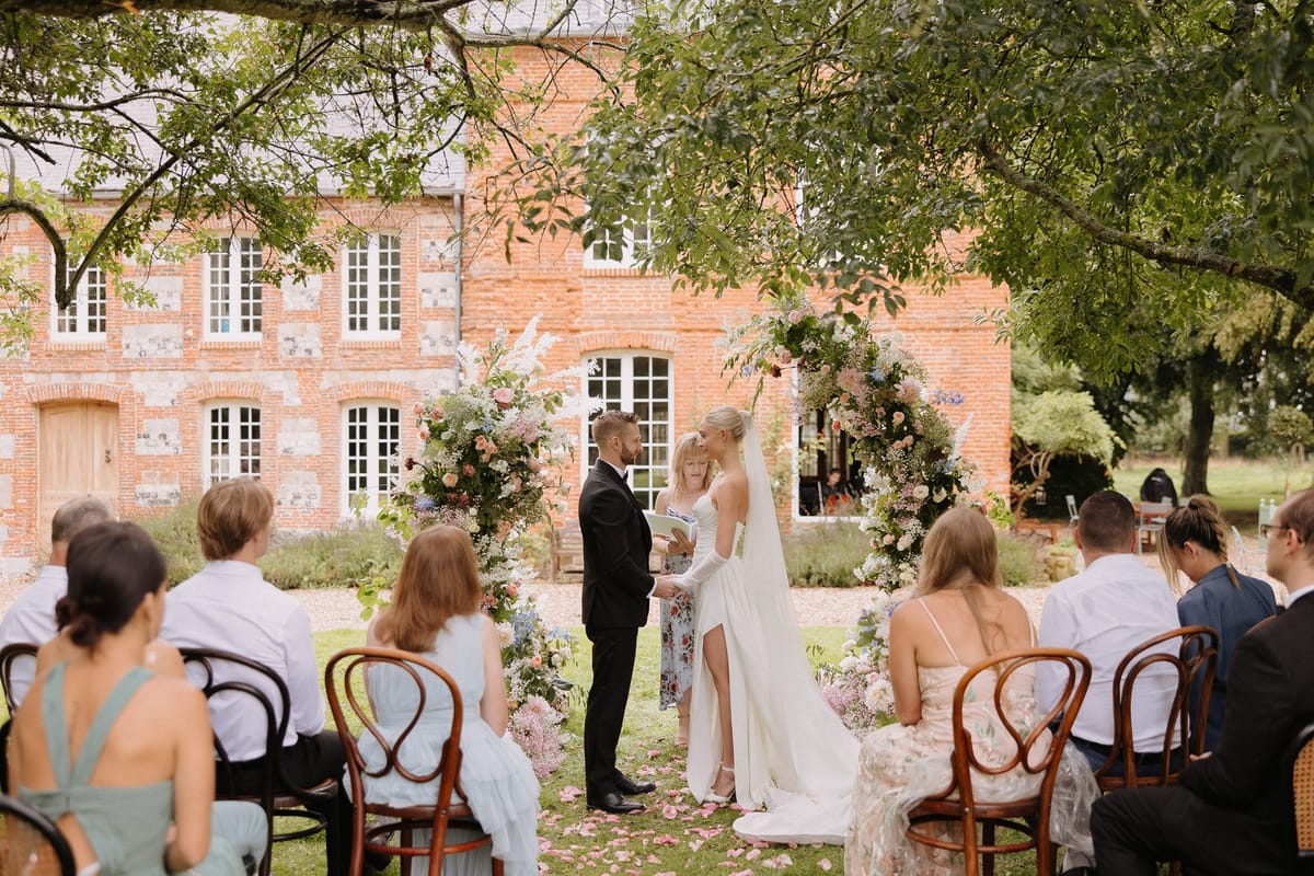 20-guest ceremony under circular floral arch with pink roses and blue accents before red brick manor