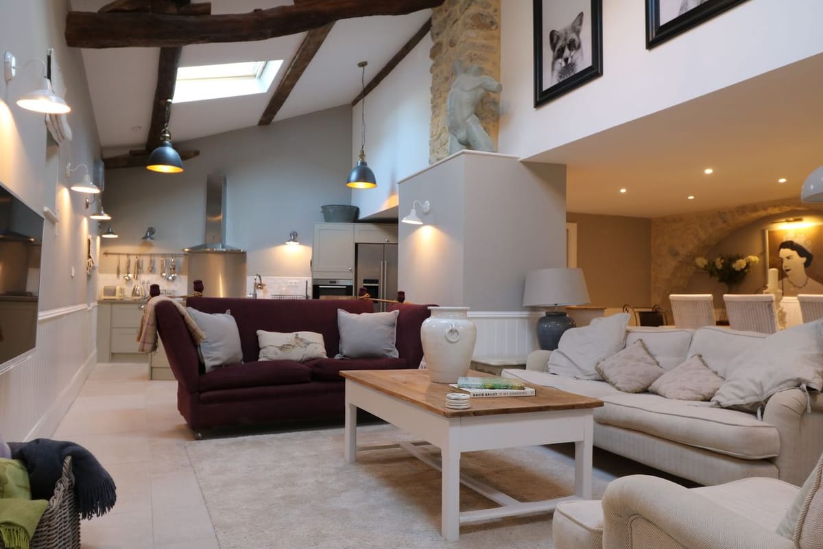 Converted barn living space with exposed beams, plum sofa, and sage green kitchen