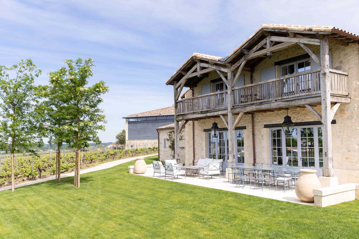 Stone and timber vineyard building with covered terrace, grapevine rows, and terracotta urns
