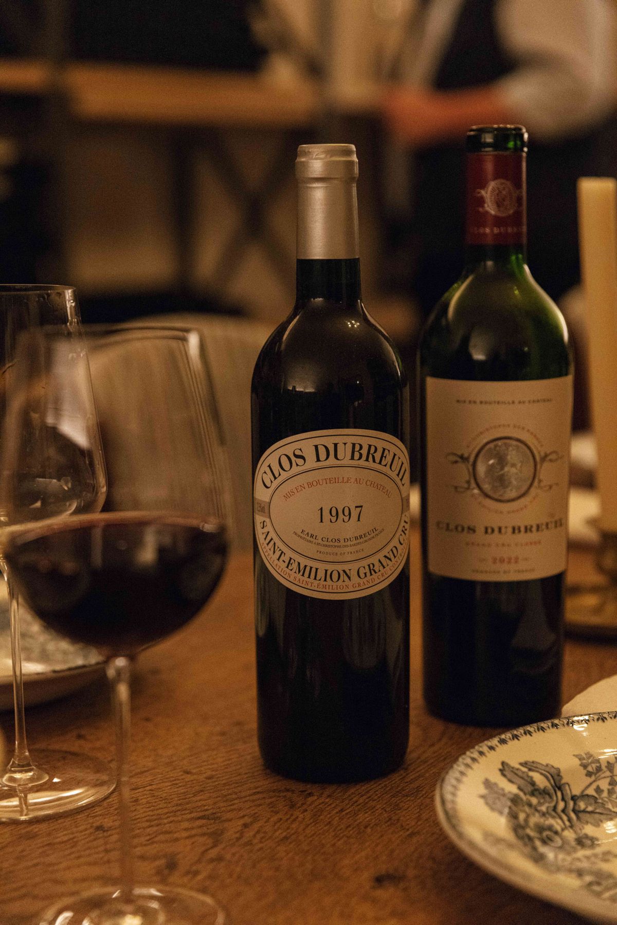 Close-up of two bottles of Clos Dubreuil Saint-Emilion Grand Cru wine with red-filled glasses on reception table
