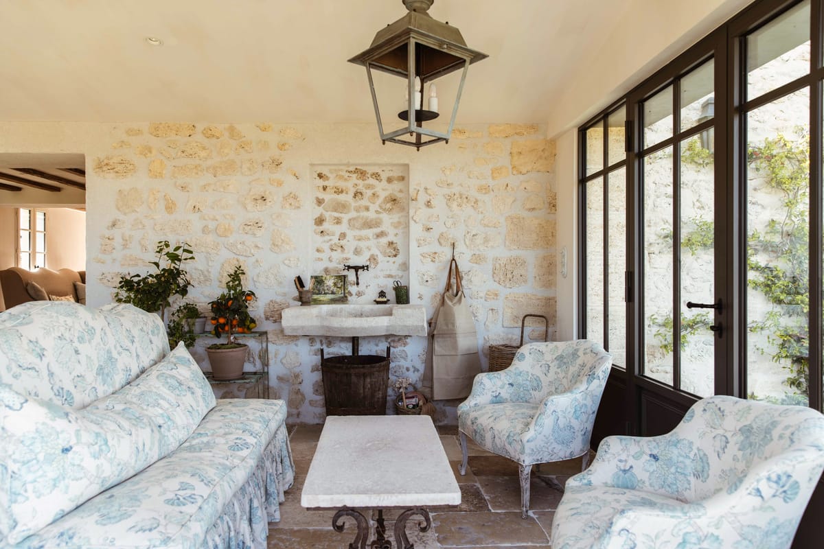 French provincial lounge with limestone walls, blue toile upholstered seating, and glass courtyard doors