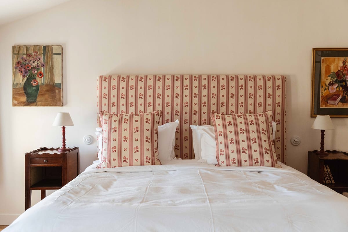 Classic French country guest bedroom with floral stripe headboard, dark wood bedside tables, and red table lamps