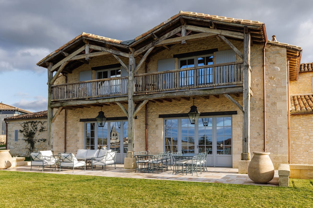 French limestone country house with timber-frame balcony, stone terrace with dining table and lounge seating