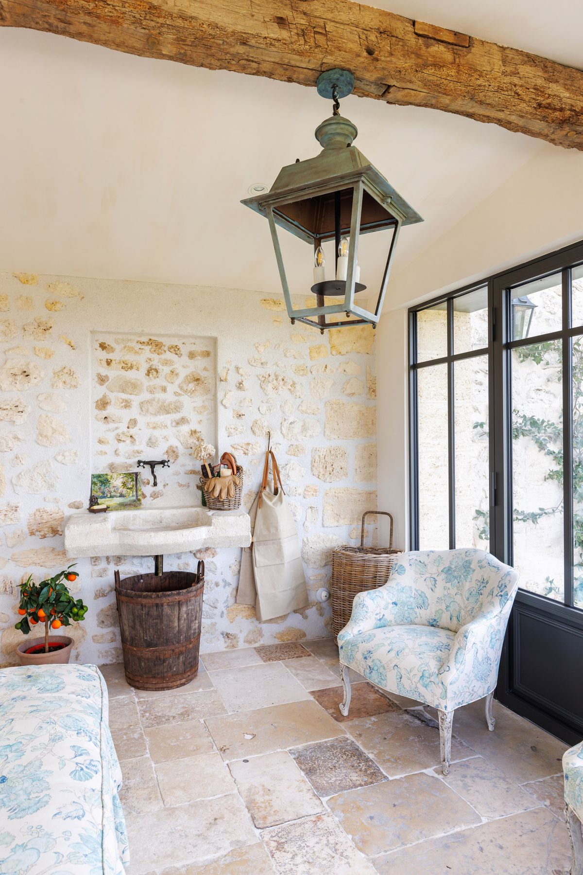 French provincial interior room with limestone walls, toile de Jouy armchairs, and steel-framed glass doors