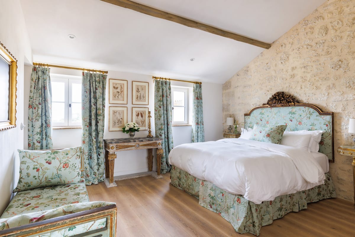 French chateau guest bedroom with gilt headboard, sage green chinoiserie fabric, botanical prints, and stone walls