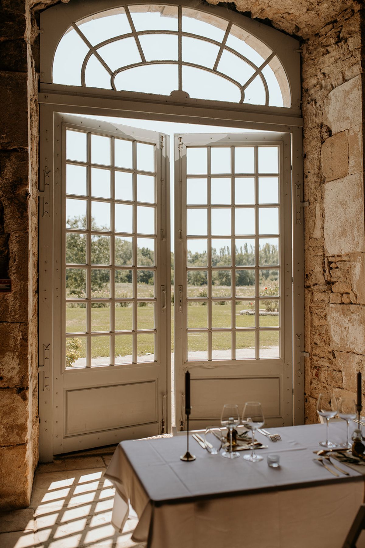 Reception table with gold cutlery and black taper candle framed by open French doors to garden