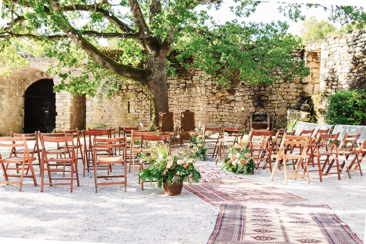 Rustic-boho ceremony in roofless stone ruin with terracotta pots, vintage rug, and string lights overhead