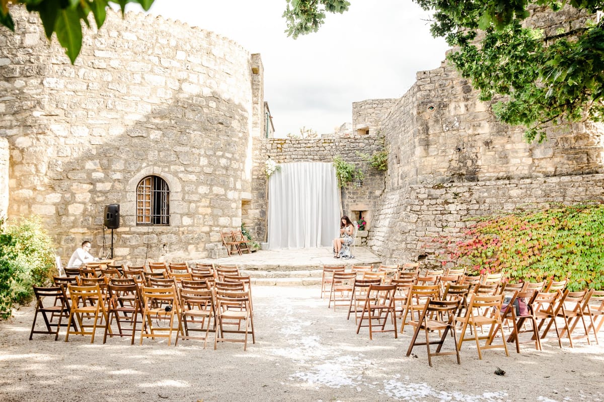 Wooden folding chairs facing white draped altar in open-air stone ruin courtyard before ceremony