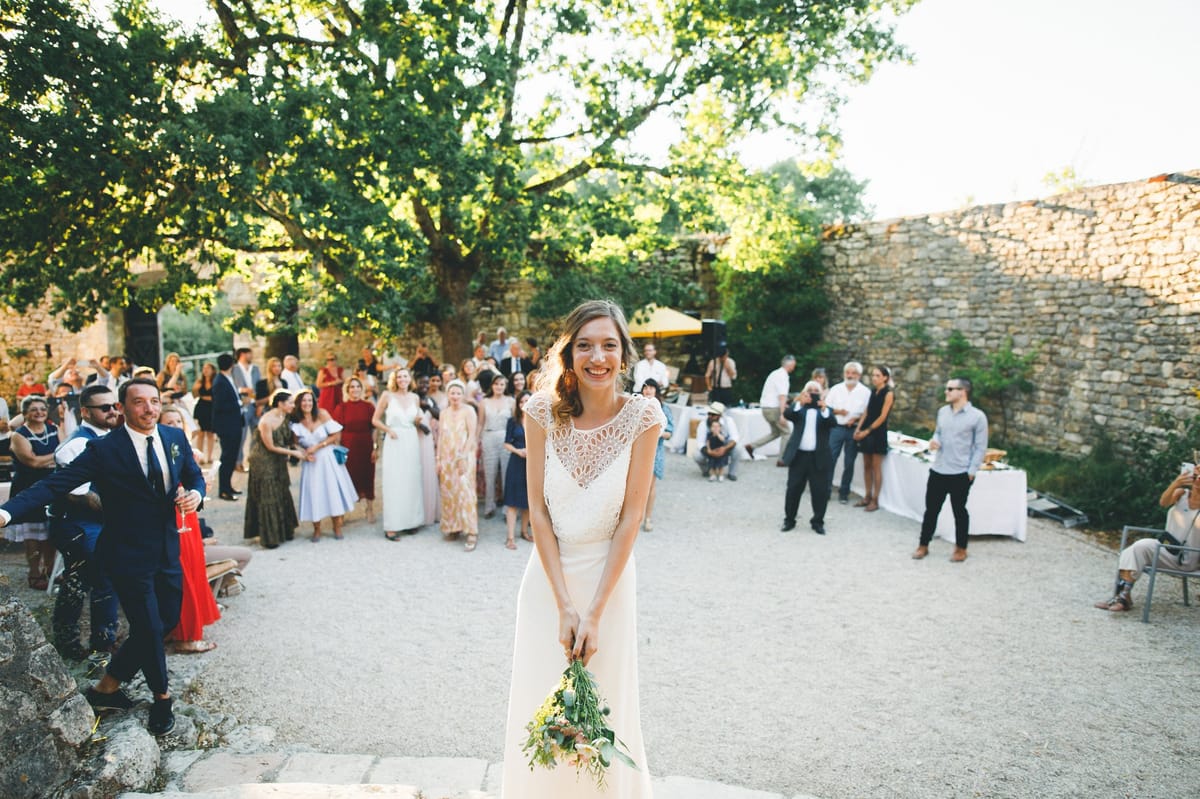 Bride smiling before bouquet toss as 40 guests gather in dry-stone walled courtyard