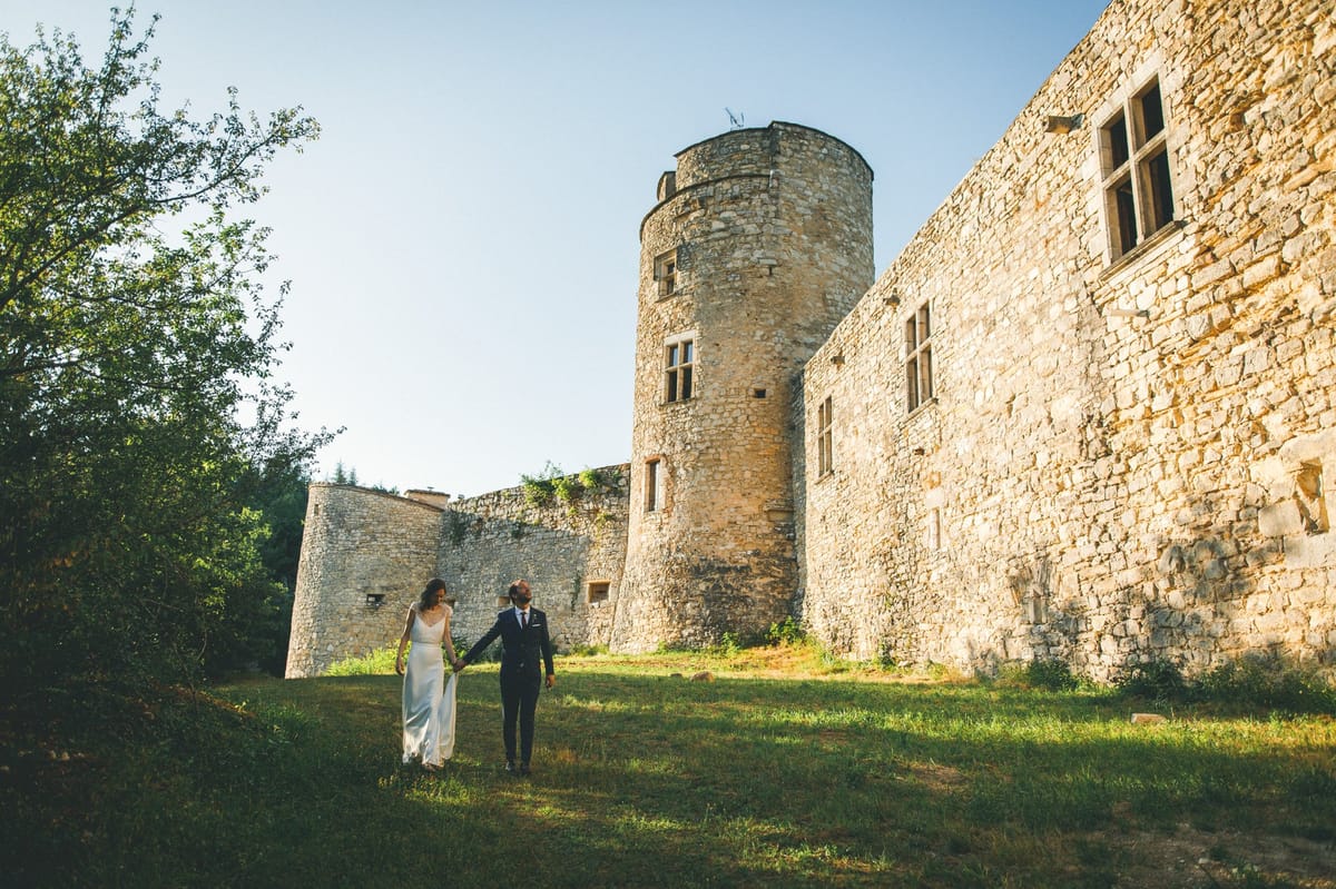 Couple walking along medieval chateau limestone walls with cylindrical tower in warm golden light