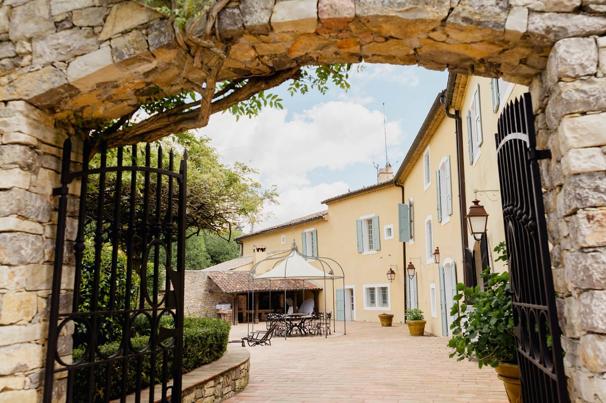Provencal bastide with ochre walls and sage shutters framed through wrought-iron gate and stone archway