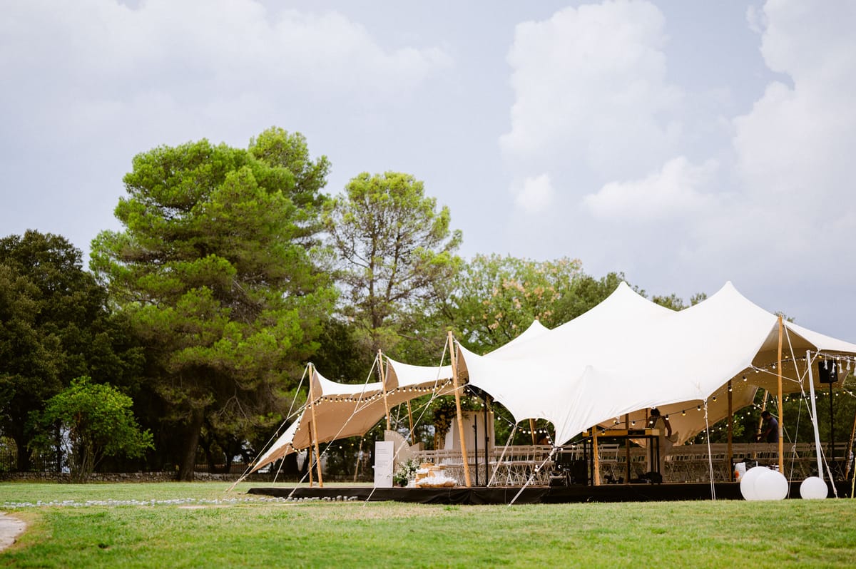 Two freeform stretch tents with festoon lights set up on lawn for outdoor wedding reception