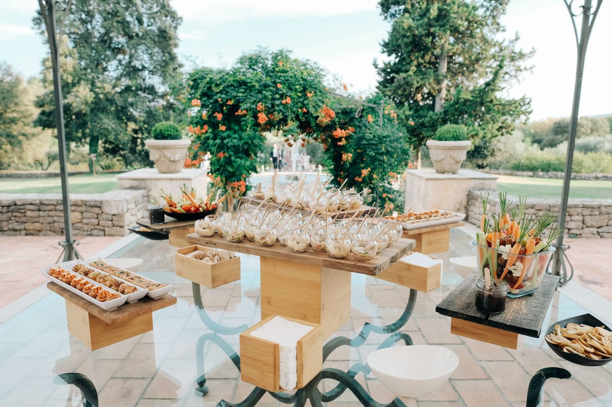 Canape station on wrought-iron table with tiered wood risers on stone terrace with formal garden beyond