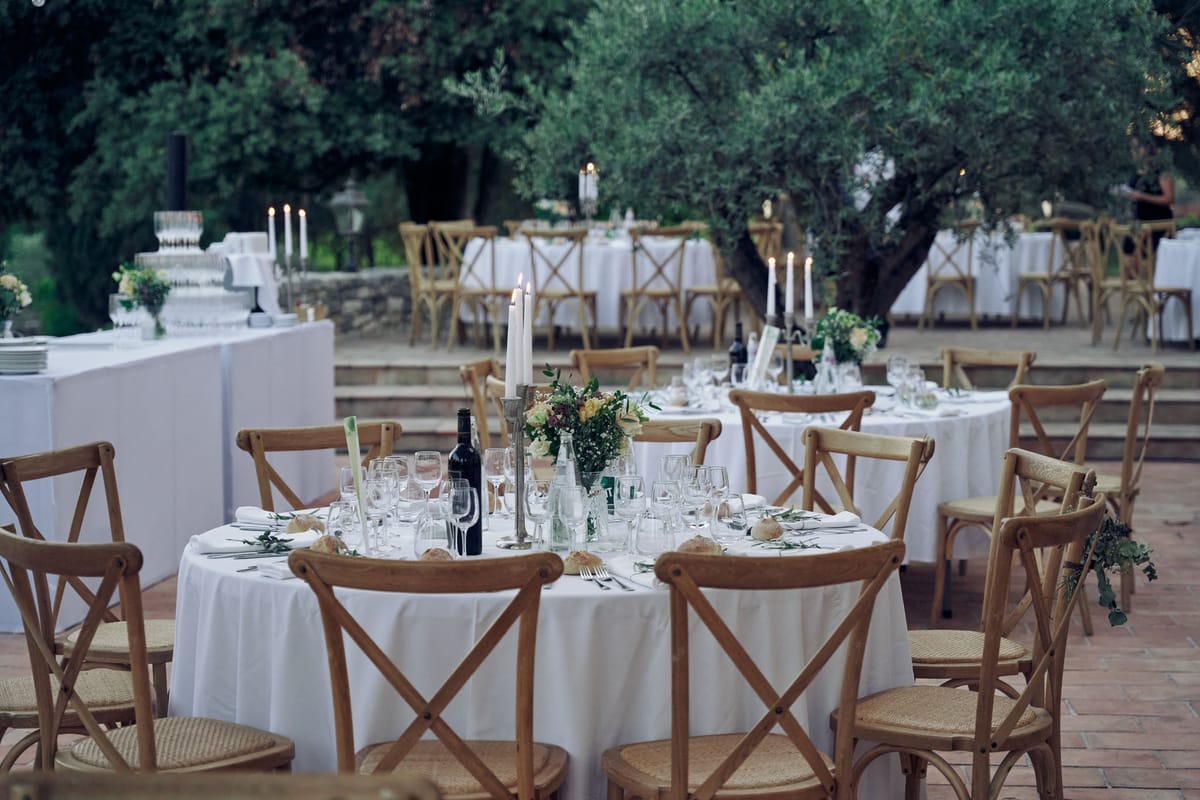 Round tables with crossback chairs, silver candlesticks, and cream florals on terracotta terrace at dusk