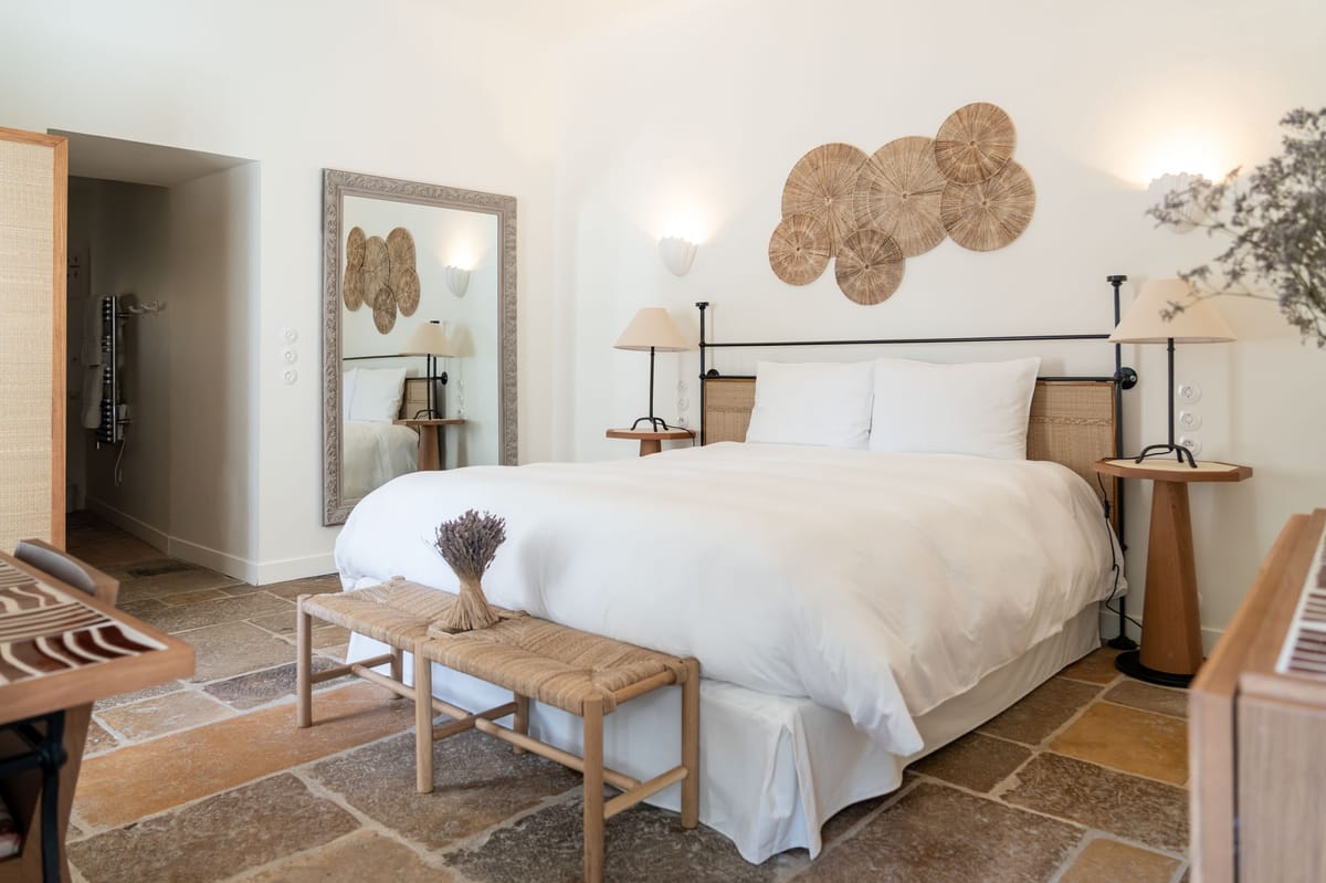 Provencal boho bedroom with rattan headboard, woven disc wall art, and terracotta tile floor