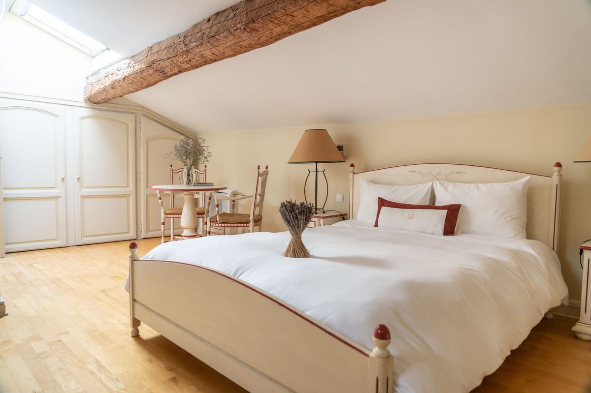 Provencal attic guest bedroom with cream and red furniture, exposed beam, skylight, and dried lavender