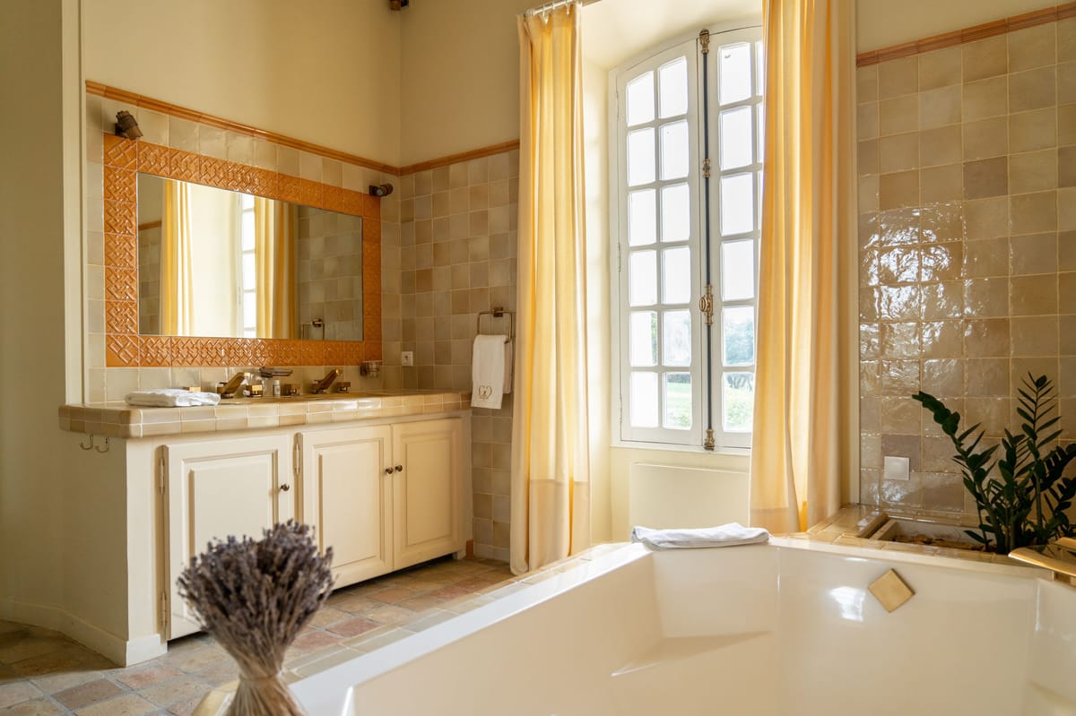 Chateau bathroom with freestanding tub, double vanity with terracotta-tiled mirror, and arched French window