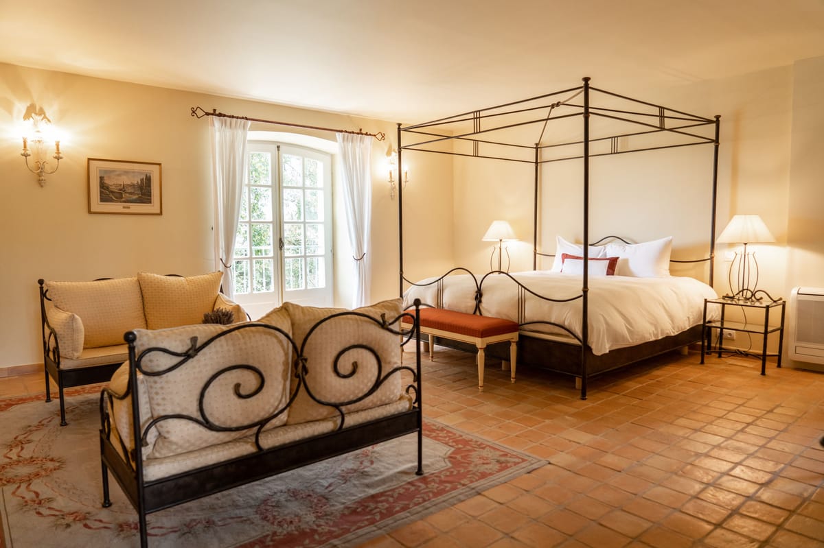 Provencal bedroom with wrought-iron four-poster bed, terracotta tiles, floral rug, and arched French window