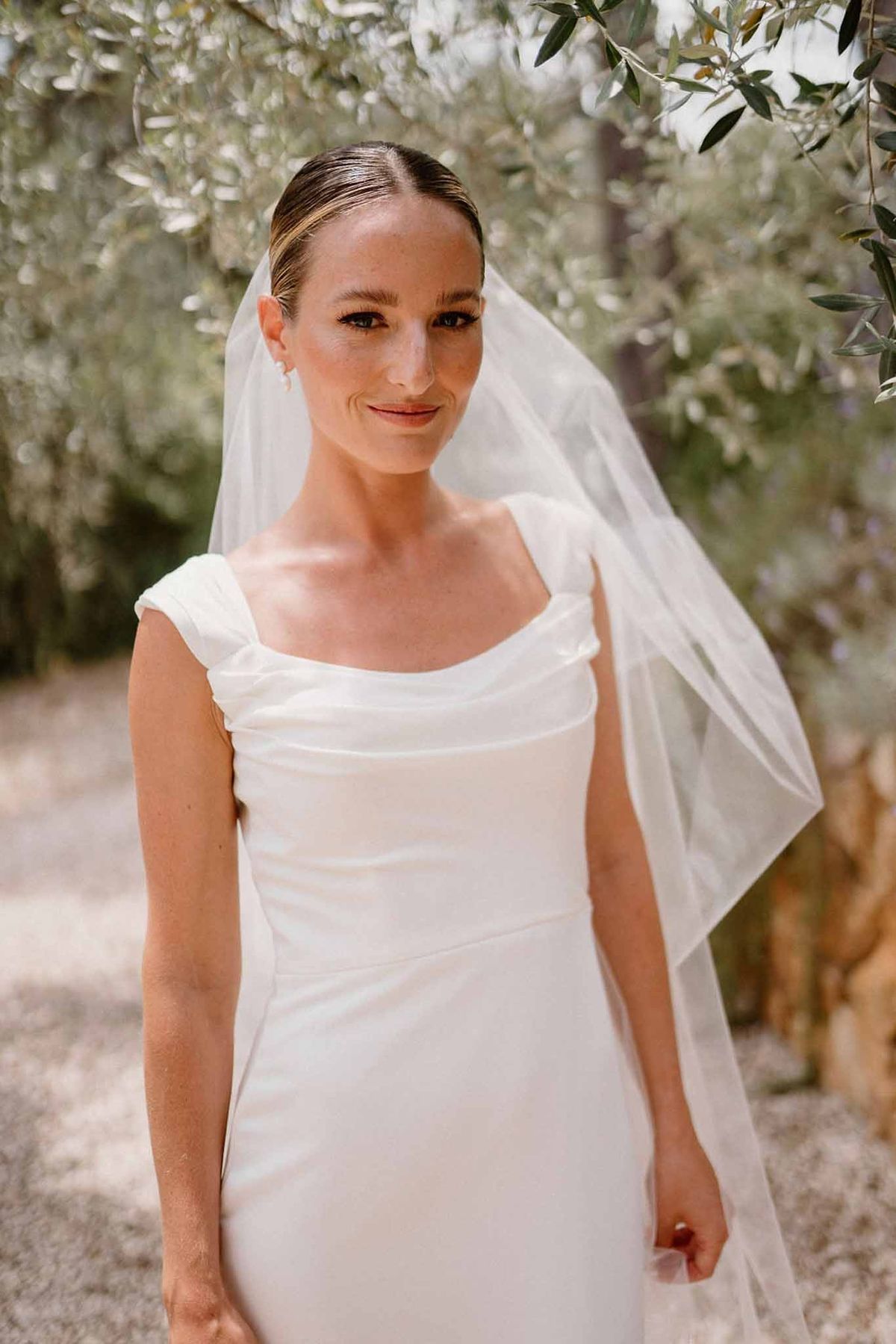 Bride in satin gown smiling under olive trees at Château Sainte-Roseline