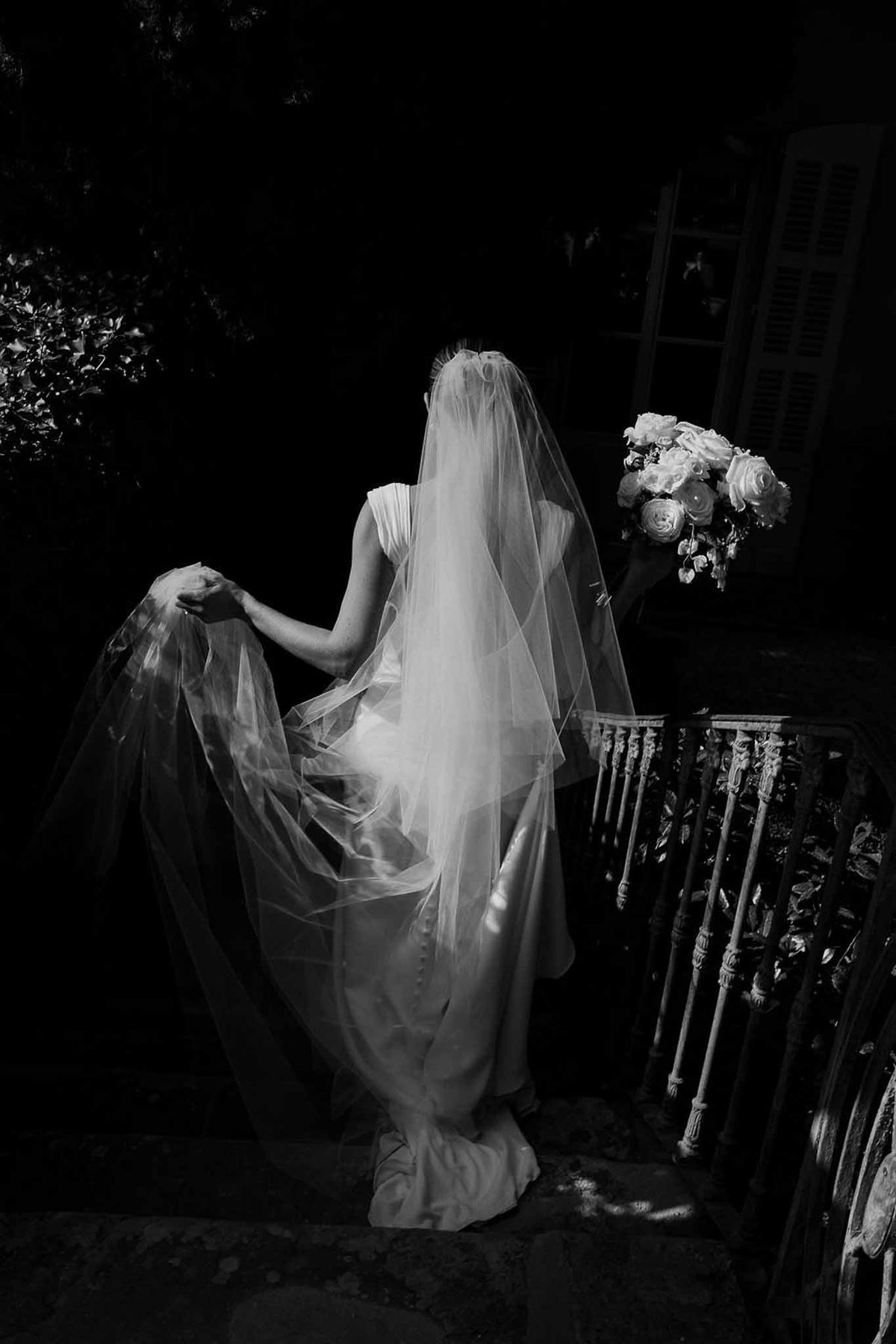 Bride descending stone steps with veil in dramatic black and white at Château Sainte-Roseline