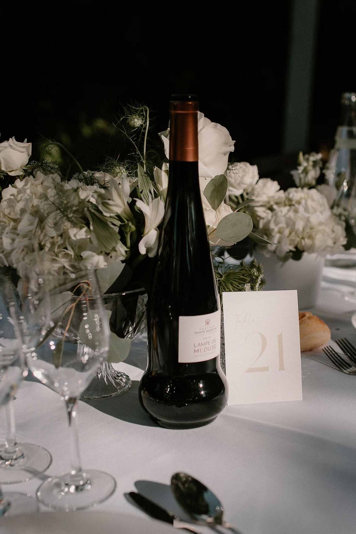 Wine bottle and gold table number with white floral centrepieces at Château Sainte-Roseline