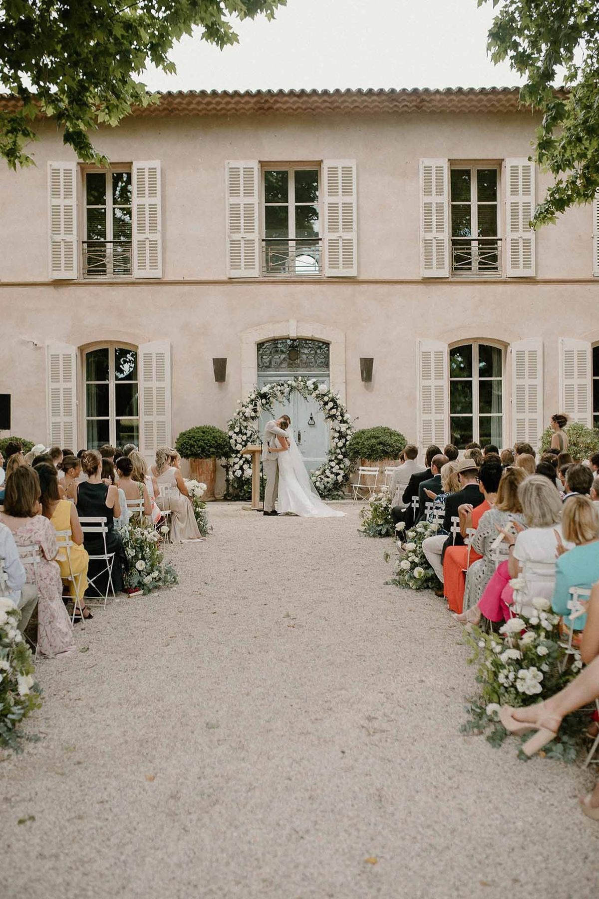 Couple at ceremony altar with pink château façade and guests at Château Sainte-Roseline