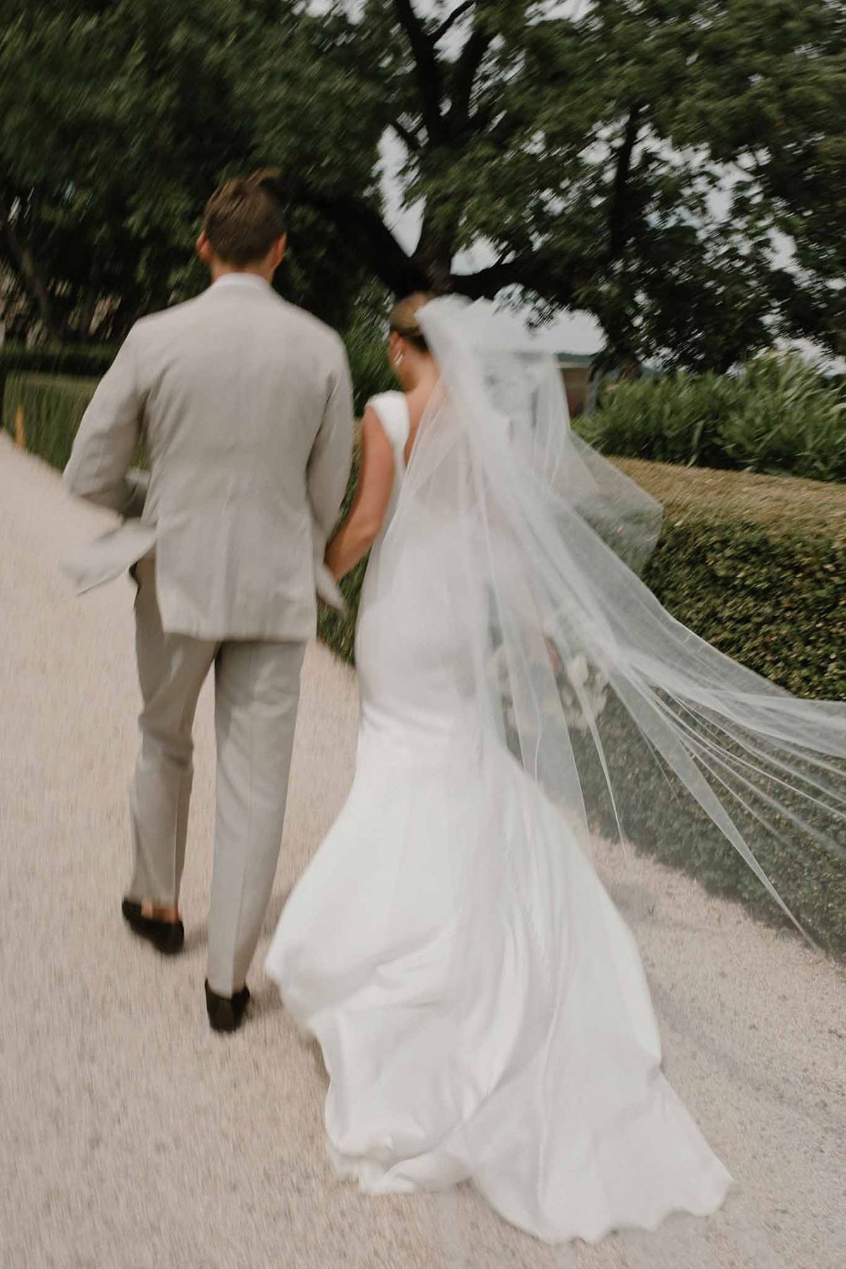 Couple walking away with veil billowing on garden path at Château Sainte-Roseline