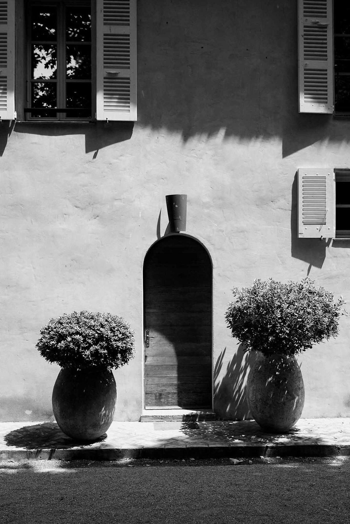 Arched doorway with terracotta planters and shuttered windows in black and white at Château Sainte-Roseline