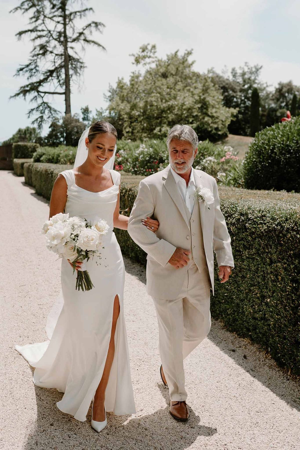 Bride and father walking on garden path between hedges at Château Sainte-Roseline
