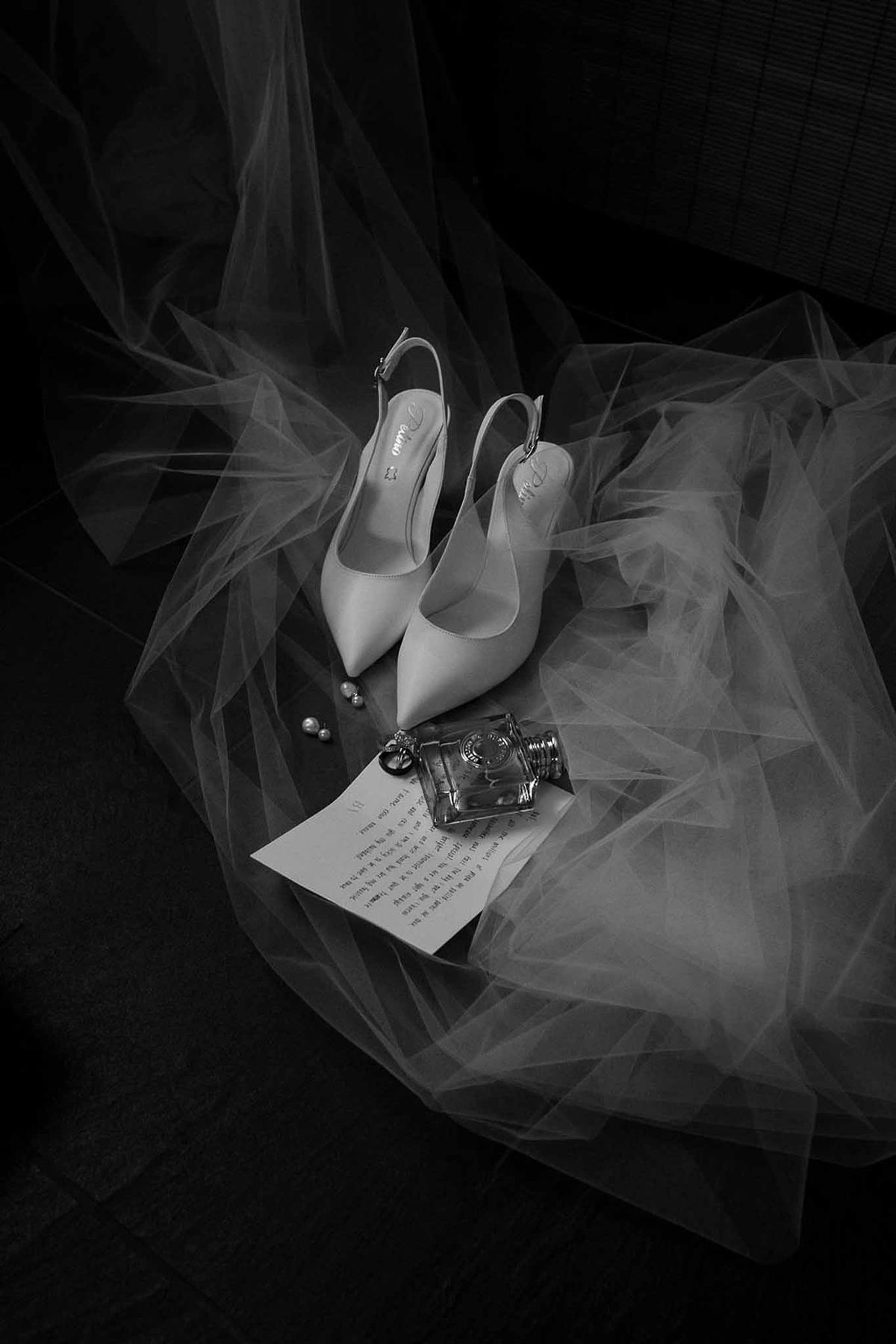 Bridal shoes, letter, perfume and earrings on veil in black and white at Château Sainte-Roseline