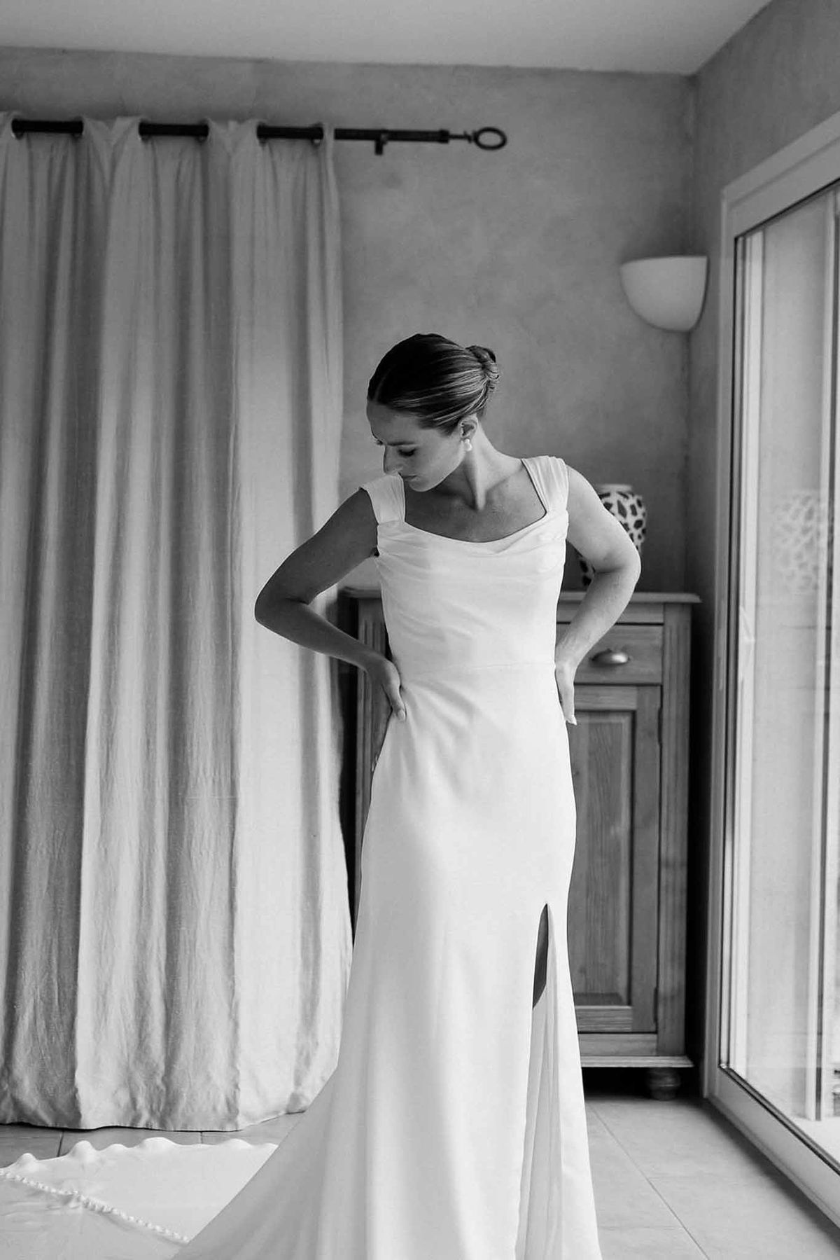 Bride in satin gown with side slit in getting ready room in black and white at Château Sainte-Roseline