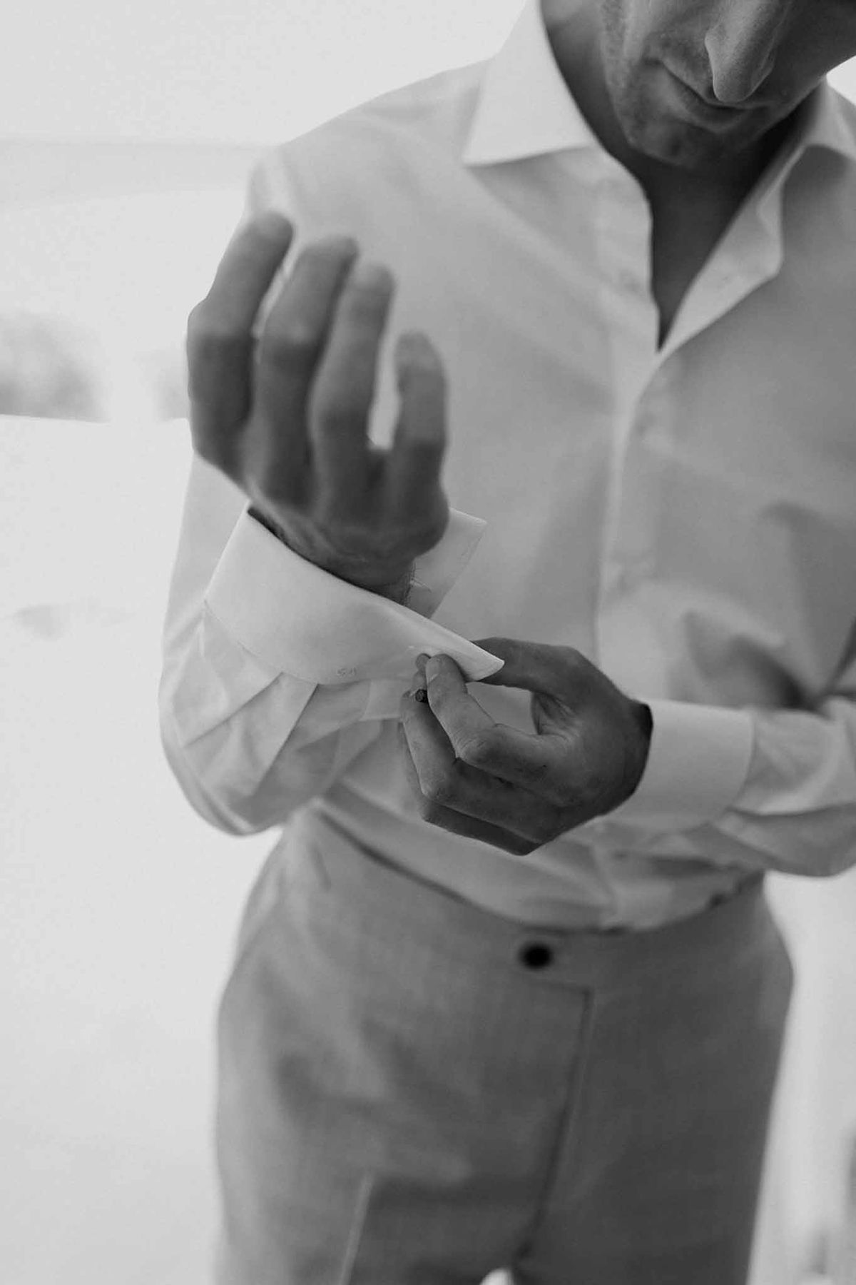 Groom adjusting shirt cuffs in black and white at Château Sainte-Roseline