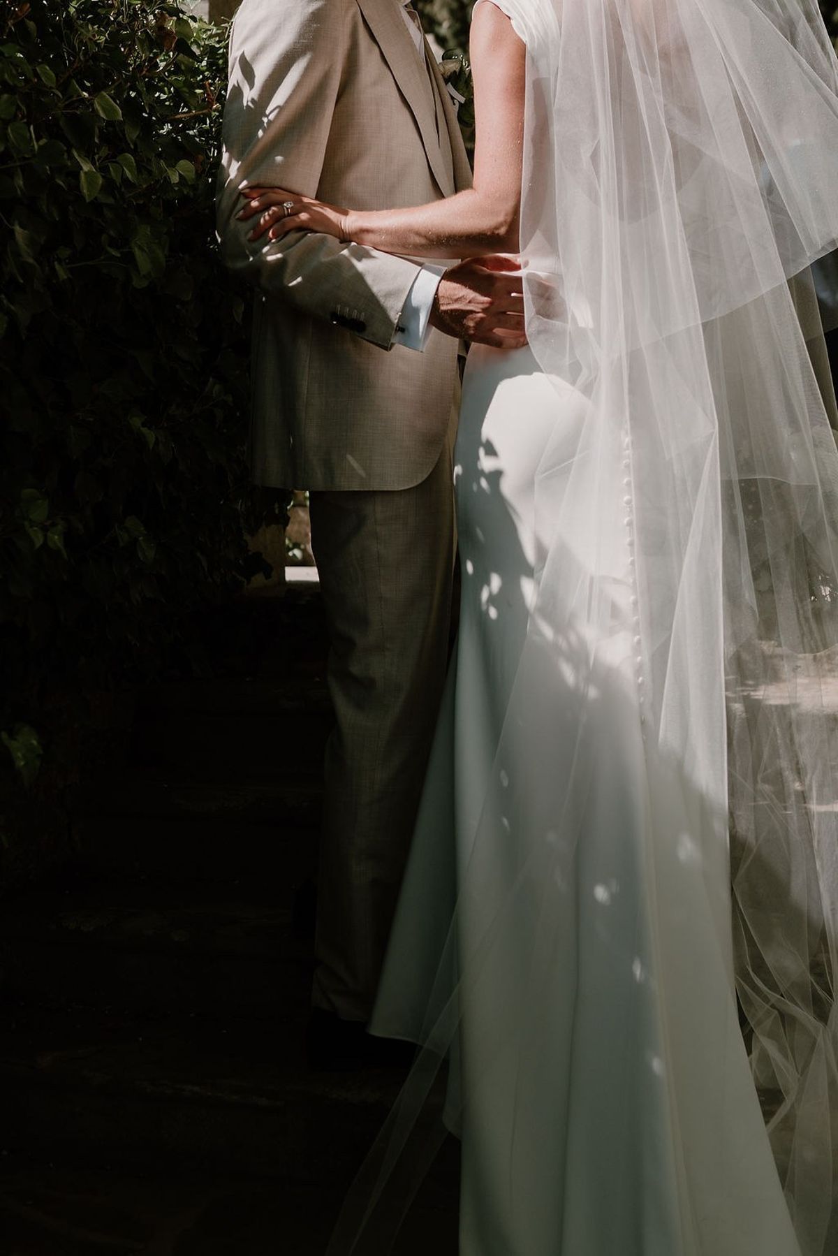 Cropped couple portrait with bride's veil and groom's linen suit in dappled light at Château Sainte-Roseline